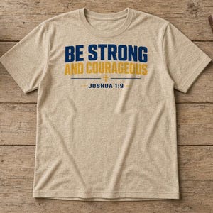 May include: A heather beige short-sleeve t-shirt featuring the dark blue and yellow text BE STRONG AND COURAGEOUS with a small cross symbol and the text JOSHUA 1:9 printed in dark blue on the front centre of the garment.