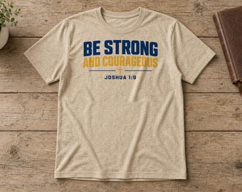 May include: A heather beige short-sleeve t-shirt featuring the dark blue and yellow text BE STRONG AND COURAGEOUS with a small cross symbol and the text JOSHUA 1:9 printed in dark blue on the front center of the garment.