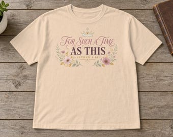 May include: A beige short-sleeve t-shirt featuring a graphic print with a crown icon, floral accents, and the text "For Such A Time As This" followed by "Esther 4:14" in a decorative script and serif font combination.