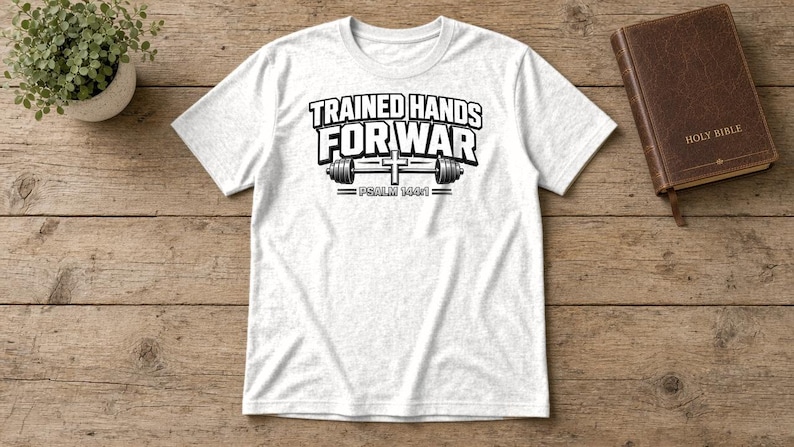 Puede incluir: Una camiseta blanca de manga corta con texto negro que dice TRAINED HANDS FOR WAR, un gr&aacute;fico de una barra de pesas con una cruz en el centro y el texto PSALM 144:1 impreso debajo del gr&aacute;fico de la barra de pesas.