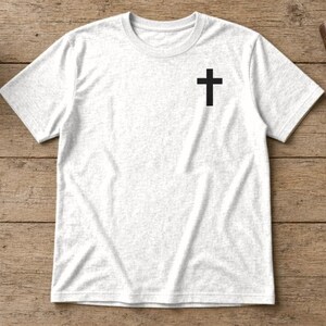 May include: A white short-sleeved t-shirt featuring a small black cross graphic printed on the upper left chest area. The shirt has a crew neckline and a heathered texture, providing a simple and clean appearance for this casual garment.
