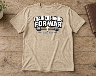 May include: A heathered beige short-sleeve t-shirt featuring the black and white text TRAINED HANDS FOR WAR with a barbell graphic and a cross in the center, followed by the text PSALM 144:1 printed on the front chest area.