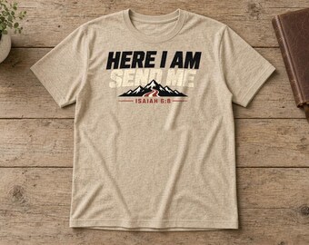 May include: A heathered beige short-sleeve t-shirt featuring the black and white text "HERE I AM SEND ME" above a graphic of black mountains with a red path, and the text "ISAIAH 6:8" underlined in red below the mountain graphic.