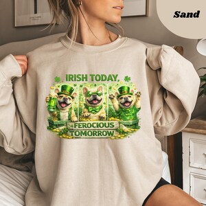 May include: A sand-colored sweatshirt featuring a graphic of three French bulldogs celebrating St. Patrick's Day. The dogs wear green hats and bow ties, with the text "Irish Today, Ferocious Tomorrow."
