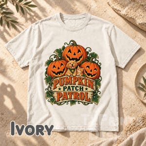 May include: An ivory short-sleeve t-shirt featuring a graphic of three orange jack-o'-lanterns, a golden retriever puppy, and a tabby kitten. The text "PUMPKIN PATCH PATROL" is printed in orange and black letters over a wooden sign illustration.