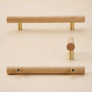 May include: Wooden cabinet pulls with brass-colored posts. The pulls are cylindrical and made of light-colored wood. The brass posts are attached to the wood. The image shows the pulls from different angles.
