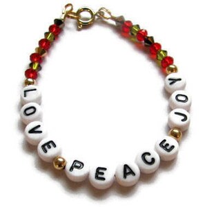 May include: A white beaded bracelet with the words "LOVE PEACE JOY" spelled out in black lettering. The bracelet is accented with gold beads and red and green crystal beads.