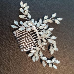 May include: A silver hair comb with a delicate design of white leaves and crystals. A single pearl is centered in the design.