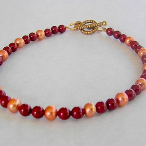 May include: A red and orange beaded bracelet with a gold clasp.
