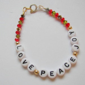 May include: A white beaded bracelet with gold spacers and red and green crystal beads. The beads spell out the words "LOVE PEACE JOY".
