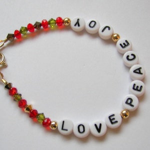 May include: A white beaded bracelet with gold spacers and red and green crystal beads. The beads spell out the words "LOVE" and "PEACE".