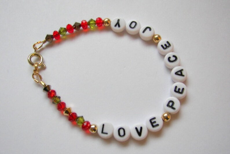 May include: A white beaded bracelet with gold spacers and red and green crystal beads. The beads spell out the words "LOVE" and "PEACE".