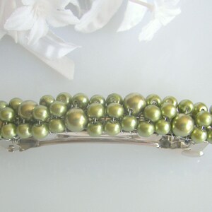 May include: A green pearl hair barrette. The barrette features multiple rows of green pearls attached to a silver-tone metal clip. The pearls vary in size, creating a textured appearance. A decorative hair accessory.