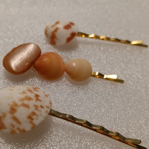 May include: Three gold hair clips with different seashell accents. The shells are in shades of brown, white, and beige.