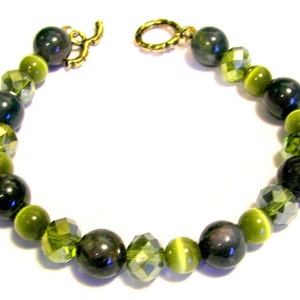 May include: A green and black beaded bracelet with a gold clasp. The bracelet features round green and black beads, as well as faceted green crystal beads.