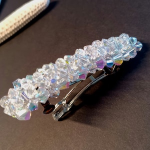 May include: A hair barrette featuring a rectangular arrangement of clear, faceted, iridescent crystals. The crystals are densely packed and attached to a silver-toned metal spring clip mechanism that allows the accessory to open and close securely.