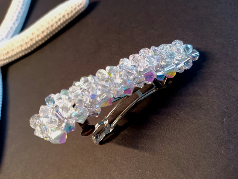 May include: A hair barrette featuring a rectangular arrangement of clear, faceted, iridescent crystals. The crystals are densely packed and attached to a silver-toned metal spring clip mechanism that allows the accessory to open and close securely.