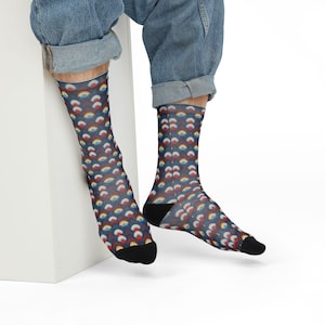 May include: A pair of socks with a navy blue background and a repeating pattern of small, colourful rainbows. The socks have black heels and toes. The person wearing the socks is sitting down.