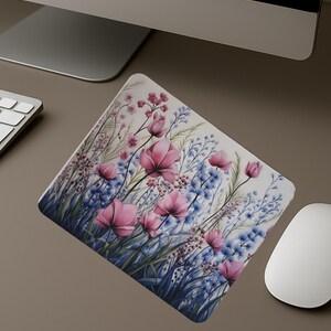 May include: A square mousepad featuring a watercolor floral design. The design includes pink flowers, blue wildflowers, and green foliage against a cream background. The mousepad is shown on a desk with a computer mouse, keyboard, and monitor.