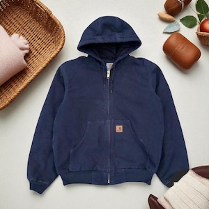 Könnte beinhalten: Marineblaue Kapuzenjacke mit durchgehendem Reißverschluss und Fronttasche. Die Jacke hat einen braunen Aufnäher auf der Vorderseite und gerippte Säume und Bündchen. Die Kapuze ist gefüttert.