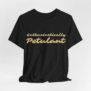 Peut inclure: T-shirt noir avec l'inscription "Enthusiastically Petulant" en lettres dorées cursives. Le t-shirt a un col rond et est fait d'un tissu doux. Un vêtement confortable et décontracté.