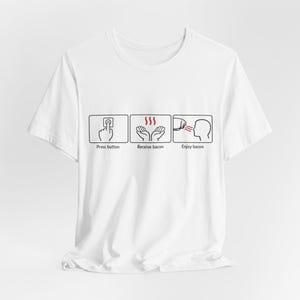 Puede incluir: Camiseta blanca con un gráfico humorístico que representa los pasos para disfrutar del tocino. El gráfico muestra una mano pulsando un botón, manos recibiendo tocino y una persona disfrutando del tocino. El texto incluye "Press button", "Receive bacon" y "Enjoy bacon".