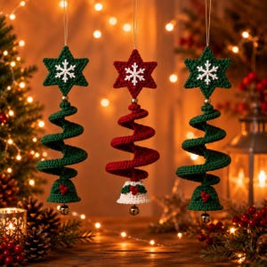 Peut inclure: Trois décorations suspendues en crochet composées d'une étoile avec un flocon blanc, d'un corps en spirale et d'une base en forme de cloche. Deux sont vertes avec des baies rouges, et une est rouge avec une cloche blanche, feuilles et baies.
