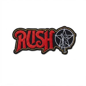 May include: An embroidered fabric patch featuring the word RUSH in bold red lettering with a gold outline. To the right of the text is a white circular emblem containing a five-pointed star and a silhouette figure, all set against a black background.