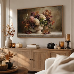 Puede incluir: Una impresión artística rectangular enmarcada que representa un bodegón al óleo de un arreglo floral en una urna de piedra. El ramo presenta flores blancas, moradas y de color óxido con hojas de otoño sobre un fondo oscuro y sombrío.