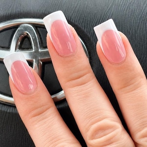 May include: A wide silver ring featuring an embossed floral pattern on the front, worn on a finger with long square-shaped nails painted in a classic French manicure style with a soft pink base and crisp white tips.