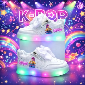 Puede incluir: Zapatillas blancas con tem&aacute;tica K-Pop con luces LED en las suelas. Los zapatos tienen una cremallera lateral, un lazo blanco y un gr&aacute;fico de dibujos animados. El fondo presenta las palabras "K-POP" y notas musicales.