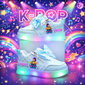 Puede incluir: Zapatillas blancas y azul claro con suela arco&iacute;ris iluminada. Los zapatos tienen un lazo en la leng&uuml;eta y un gr&aacute;fico de un personaje de dibujos animados. El texto "K-POP" y "Demon Hunters Rumi" es visible.