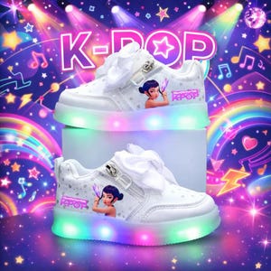 Puede incluir: Zapatillas blancas con tem&aacute;tica K-Pop con luces LED de colores en las suelas. Los zapatos presentan un gr&aacute;fico de dibujos animados de una ni&ntilde;a y el texto "K-POP". Tienen lazos blancos y cierre de cremallera.