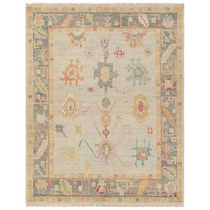 May include: Rectangular area rug with a light blue central field and a dark gray border. The rug features a complex pattern of floral and geometric designs in shades of orange, pink, yellow, and teal. The rug has a fringe along the edges.