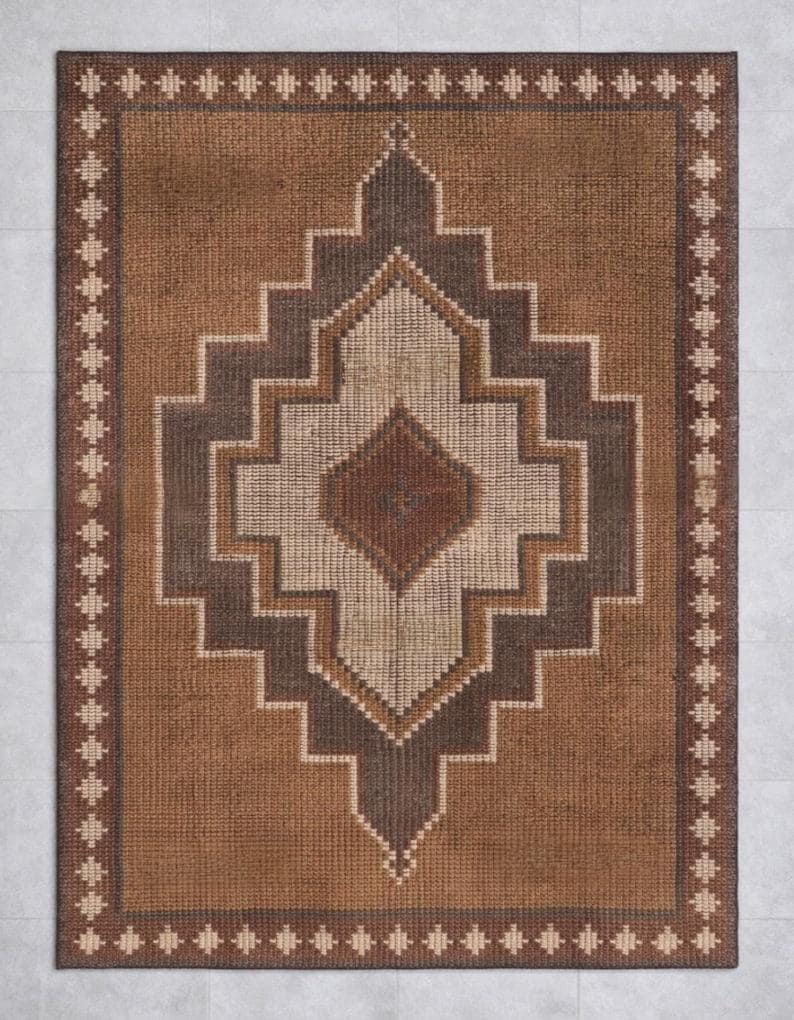 May include: A rectangular brown rug with a geometric diamond pattern in shades of brown and beige. The rug has a border with a repeating pattern of small, stylized shapes.