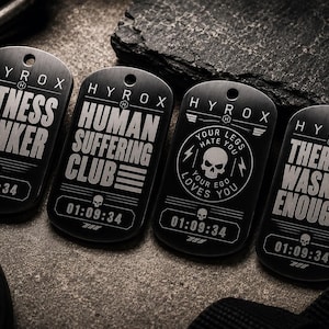 May include: Four black dog tags with white text and a skull graphic. The tags read "FITNESS WANKER", "HUMAN SUFFERING CLUB", "YOUR LEGS HATE YOU, YOUR EGO LOVES YOU", and "THERAPY WASN'T ENOUGH". Each tag has the time "01:09:34".