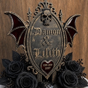 May include: A decorative oval plaque with a distressed gold and black finish, featuring a skull at the top, bat wings on the sides, and the text "Damon & Lilith" above a heart-shaped insert with the date "13th July 2027" surrounded by black roses.