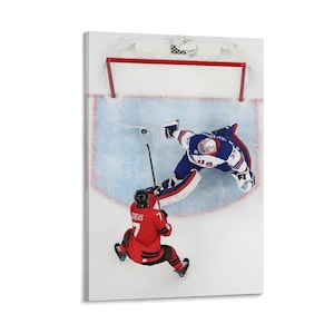 Op de afbeelding: Een canvas print van een ijshockeywedstrijd. Twee spelers zijn in beeld, een in een rood uniform en de andere in een blauw uniform. De rode speler probeert te scoren, terwijl de blauwe speler verdedigt.