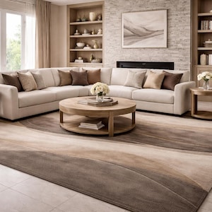 May include: A modern living room featuring a large, off-white sectional sofa with several throw pillows in shades of brown. A round wooden coffee table sits in front of the sofa, and a patterned rug in neutral tones covers the floor. The room has a fireplace and built-in shelves.