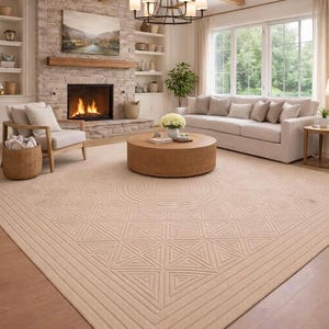 May include: A beige geometric patterned area rug in a living room setting. The rug features a repeating triangle and circle design. The room includes a fireplace, sofa, and a round coffee table. The room has a neutral color palette.