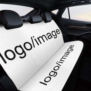 Op de afbeelding: Witte autohoes met de tekst "logo/image" in zwart. De hoes bevindt zich in een auto-interieur met zwarte hoofdsteunen en bekleding. Eenvoudig en modern ontwerp.