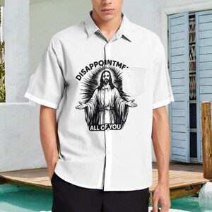 May include: White short-sleeved button-down shirt with a chest pocket. The shirt displays a black and white graphic of a religious figure with the text "DISAPPOINTME ALL OF YOU".