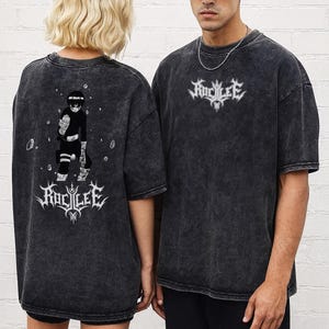 May include: Two dark gray t-shirts with a faded, textured appearance. One shirt features a graphic of a character and the text "ROC LEE" in white. The other shirt has the same text in white. Both shirts have short sleeves.