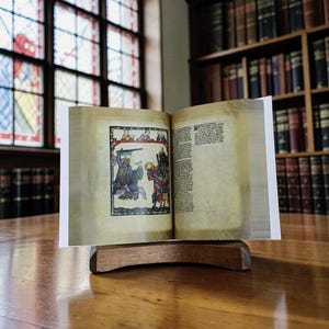 May include: An open antique book with colorful illustrations, displayed on a wooden stand. The pages show medieval artwork, with a knight on horseback and figures in detailed attire. The background includes a library setting with bookshelves and a stained-glass window.