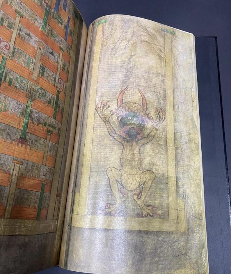 May include: Open book with a detailed illustration of a horned, green-faced creature with outstretched arms. The creature is depicted in a seated position, with a yellow border around the image. The opposite page shows a detailed architectural drawing.