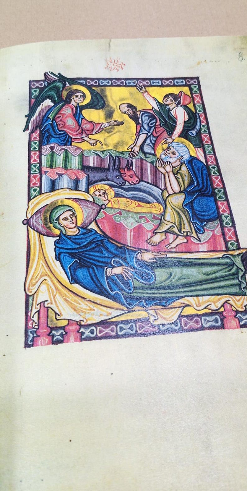 Może przedstawiać: Strona z iluminowanego manuskryptu przedstawiająca scenę religijną. Dzieło sztuki przedstawia postacie w kolorze niebieskim, czerwonym i złotym, w tym anioła, osobę w ł&oacute;żku i inne postacie. Styl przypomina sztukę średniowieczną.