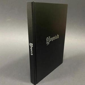 May include: A black hardcover book with the word "Voynich" in silver lettering on the cover and spine. The book is standing upright against a gray background. The text is in a gothic font.