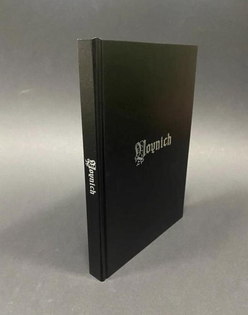 May include: A black hardcover book with the word "Voynich" in silver lettering on the cover and spine. The book is standing upright against a gray background. The text is in a gothic font.