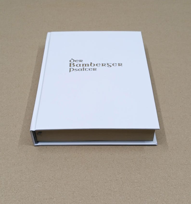 Może przedstawiać: Książka w twardej oprawie z białą okładką. Tytuł "Der Bamberger Psalter" jest wydrukowany złotą czcionką na okładce. Książka jest zamknięta i spoczywa na powierzchni w neutralnym kolorze.