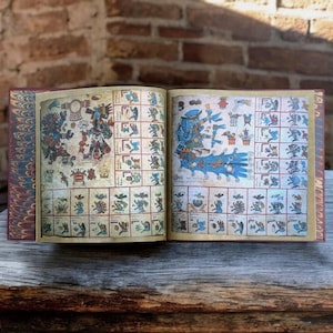 May include: An open book with pages displaying colourful illustrations and glyphs. The book's cover is a deep red with a patterned design. The pages feature detailed drawings in shades of blue, red, and yellow, with intricate patterns and figures.